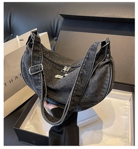 Detail of dark grey denim hobo bag with silver zippers and adjustable strap in a gift box