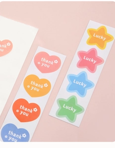 Flat lay of heart and star stickers with Thank You and Lucky text on pink background