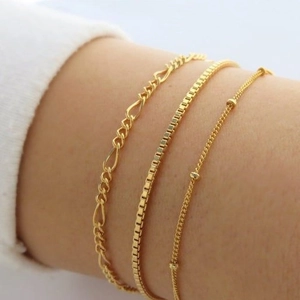 Dreiteiliges vergoldetes Armband-Set mit Figaro- und Box-Ketten am Handgelenk einer Frau