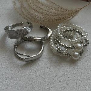 Detailed view of layered silver bangles with metallic beads and white pearls on white texture