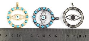 Detailed view of Evil Eye round pendants in various finishes with a ruler for size scale