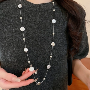 French vintage long necklace with acrylic pearls and silver metal charms on a grey sweater