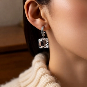 Close-up of silver C-shaped earrings with emerald-cut crystal on a model wearing a sweater