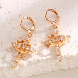 Macro shot of gold cross hoop earrings with sparkling cubic zirconia on a stone surface