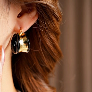 Gros plan d'une boucle d'oreille créole en émail noir doré portée par un mannequin