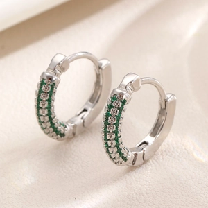 Silver hoop earrings with double-row emerald green zircons on textured background