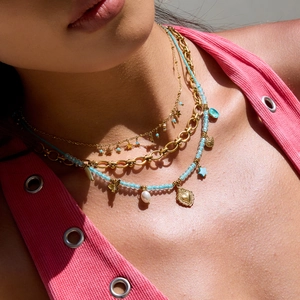 Close-up of layered gold chains and blue beaded necklace with heart and butterfly charms