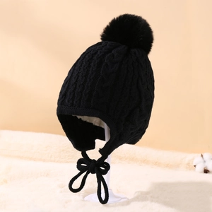 Close-up of black cable knit baby winter hat with large pompom and earflaps