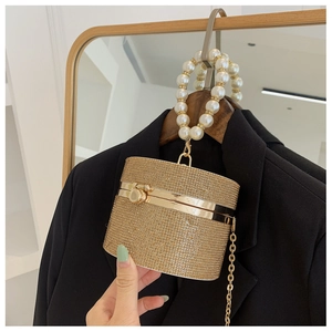 Detail of a gold glitter evening bag featuring a large pearl handle and metal chain strap