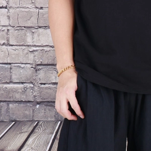 Close-up of a gold Cuban link chain bracelet worn by a male model in industrial setting