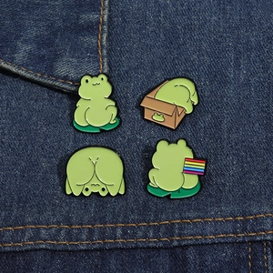Set of four cute cartoon frog enamel pins displayed on blue denim fabric background
