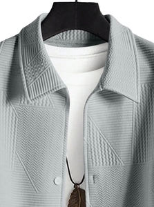 Close-up of light grey textured jacket collar with 3D geometric pattern and feather necklace