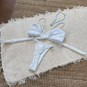 Flat lay of white bikini set with gold V-hardware and blue beaded necklace on woven rug
