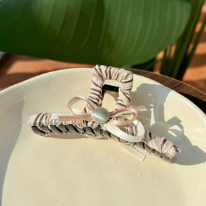 Striped fabric hair claw clip with bow decoration on a ceramic plate for women