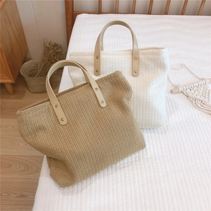 Detail of woven tote bags with leather handles and gold rivets on white bedding