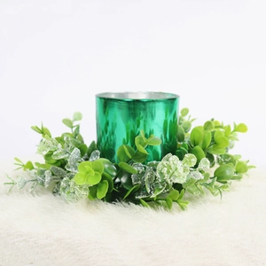 Detail view of a green metallic candle holder with decorative eucalyptus leaves on white fur