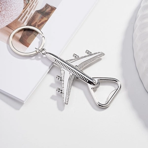 Silver metal airplane shaped bottle opener keychain shown from a top-down view on a desk