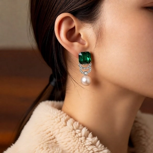 Detail view of emerald crystal and pearl drop earrings worn on a model in warm light