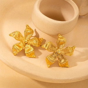 Detailed view of gold flower earrings with delicate textured petals on beige ceramic