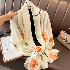 Elegant ivory silk scarf with red rose print and green leaves on a luxury leather sofa