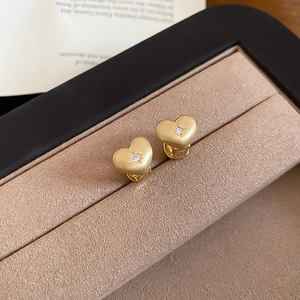 Close-up of golden heart-shaped zircon earrings with matte finish and starburst setting