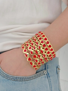 Gros plan de bracelets élastiques dorés ornés de cœurs en émail rouge et cerises