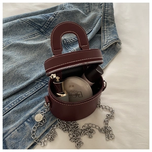 Détail du sac seau cylindrique bordeaux avec chaîne argentée sur fond de jean denim