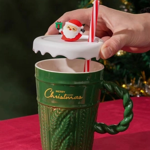Close-up of green ceramic Christmas mug with knit texture, Santa lid and striped straw