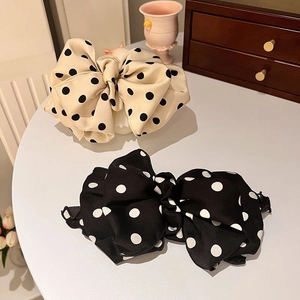 Close-up of double-layer polka dot bow hair clips in beige and black on a white table