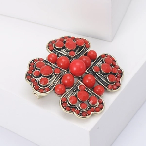 Vintage bronze four-leaf clover brooch featuring red beads on a white pedestal display