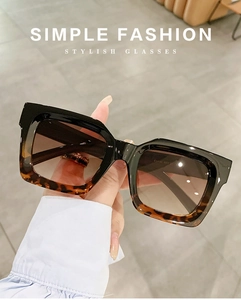Detail van hand die stijlvolle vierkante oversized zonnebril vasthoudt met bruin verloop