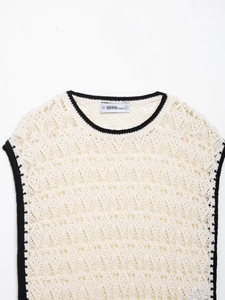Détail du gilet en maille crème avec bords contrastés noirs et texture ajourée fine