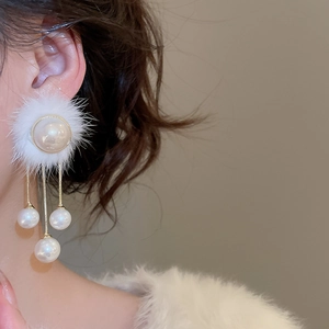 Detail of elegant white pompom and pearl tassel earrings shown on a model