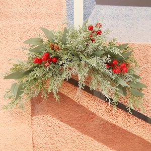 Christmas door swag with green pine needles, red berries and pine cones on a wall