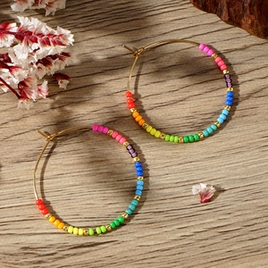 Detail shot of bohemian golden hoop earrings with colorful rainbow seed beads on wood