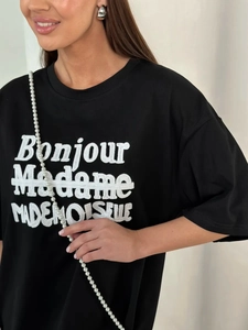 Close-up of black cotton T-shirt featuring white letter embroidery and pearl strap detail