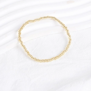 Detail of minimalist golden bead strand bracelet laid on a white textured fabric surface