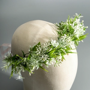 Close-up of realistic white fabric flowers and green leaves on a bridal wreath crown