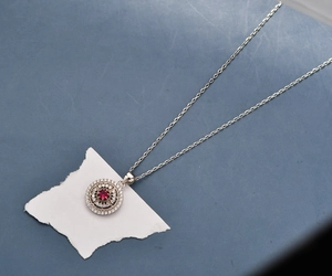Macro detail of round pendant with red ruby and double halo of white diamonds