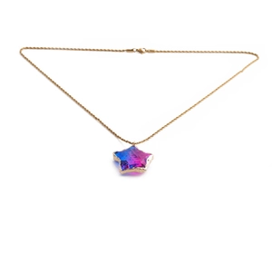 Macro-opname van gouden ketting met sterhanger en blauw-roze-paarse edelsteen