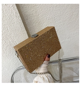 Close-up of golden glitter box clutch with metallic silver chain strap and snap closure