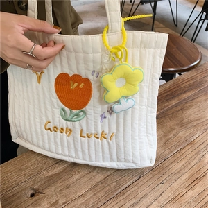 Detail of white quilted tote bag featuring tulip embroidery and yellow flower charm