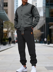 Detail of grey baseball jacket and black joggers with cream drawstrings in urban setting