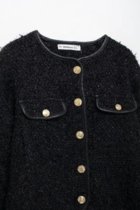 Gros plan d'une veste en tweed noir avec boutons dorés et détail de l'étiquette