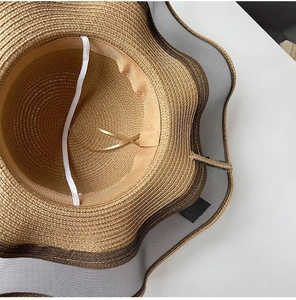 Detail of woven straw hat featuring a wavy mesh edge and white elastic chin strap