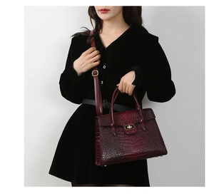 Detail view of burgundy crocodile pattern handbag with gold twist lock and black dress