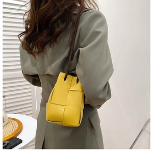 Detail of yellow woven bucket bag with thin brown shoulder strap worn by a model