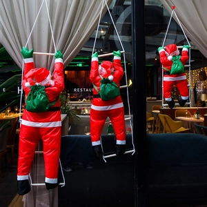 Dettaglio di tre figure di Babbo Natale che salgono una scala di corda per decorazione