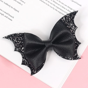 Detailed view of black glitter bat wing hair bow clip on a vintage book page backdrop