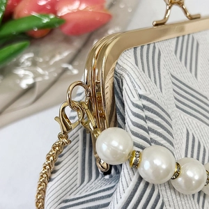 Detailed macro view of golden ball clasp and pearl handle on pleated shell clutch bag